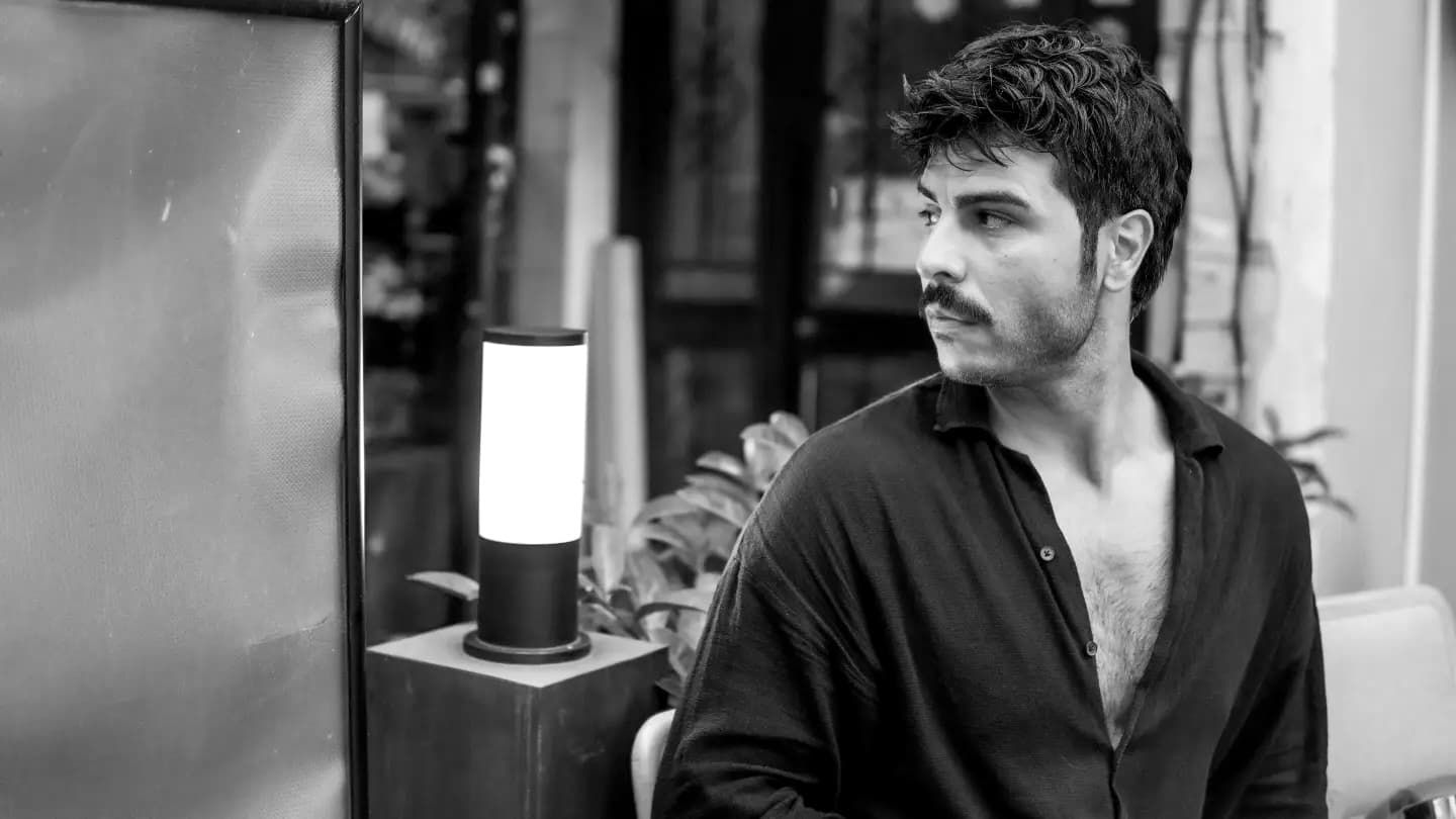 Man with a mustache looking away in a black and white cafe setting.