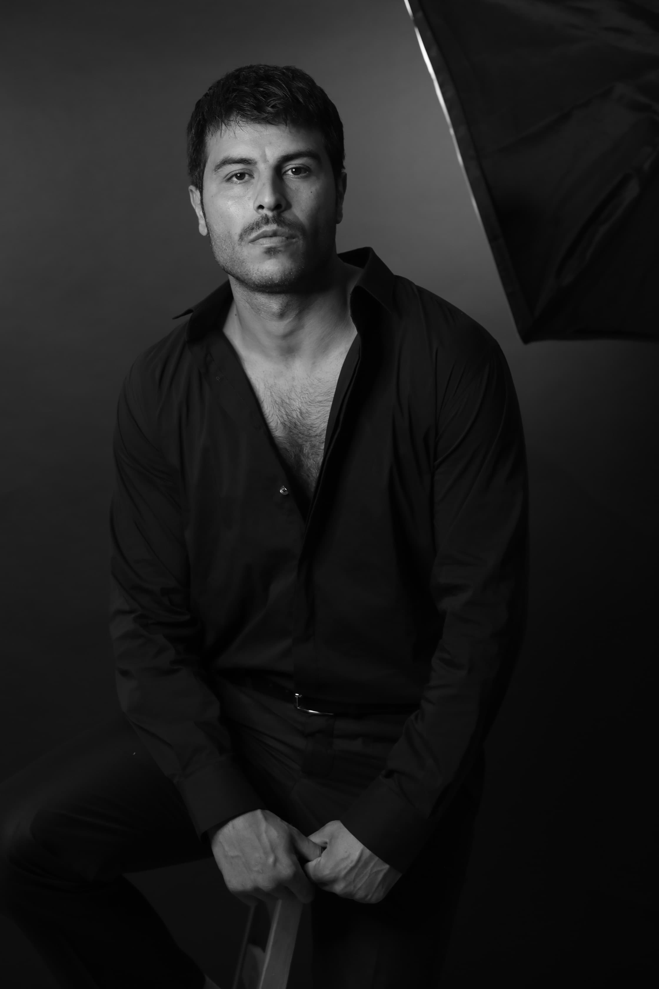 Dramatic black and white studio portrait of a man wearing an unbuttoned dark shirt.