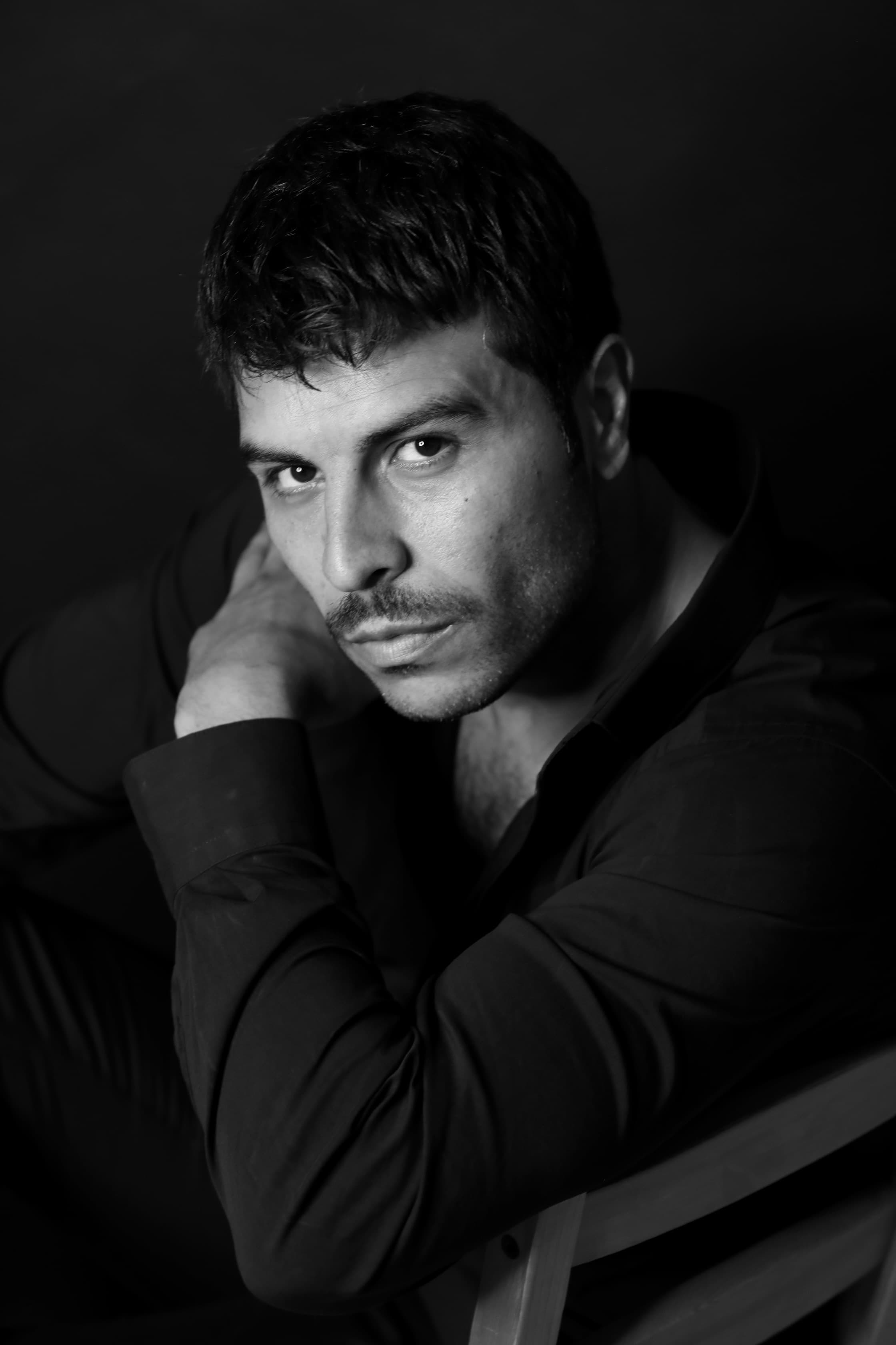 Intense black and white portrait of a man with a mustache leaning on his arm.