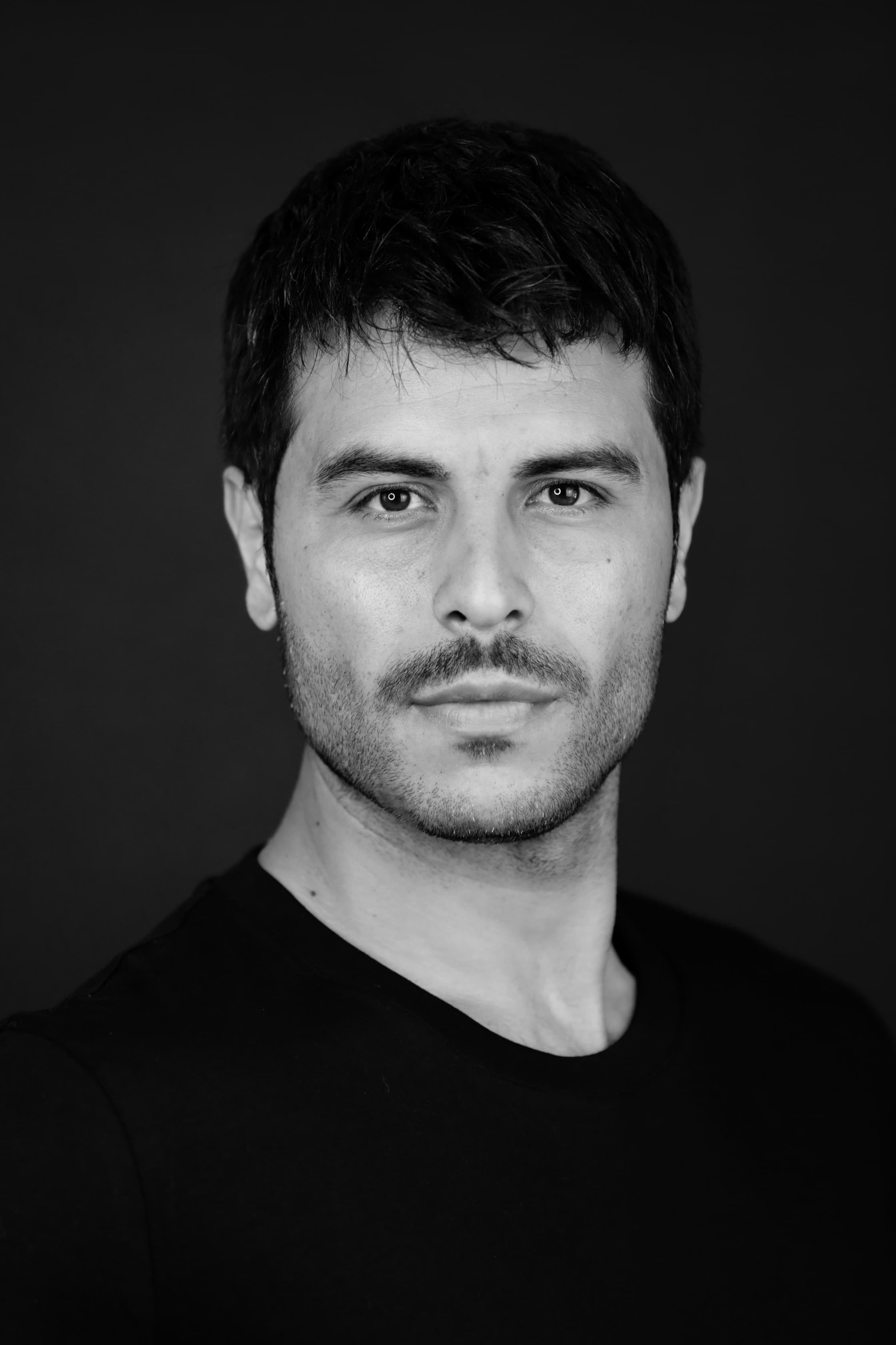 Black and white headshot of a man with short dark hair, mustache, and light stubble.
