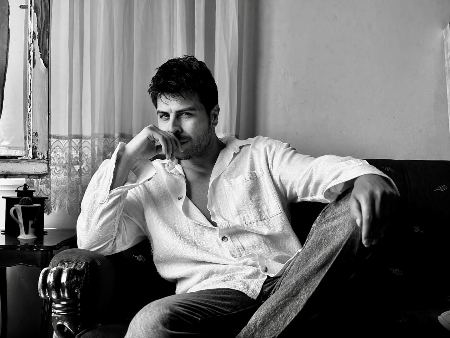 Man in a white shirt sits on a sofa in a black and white portrait.