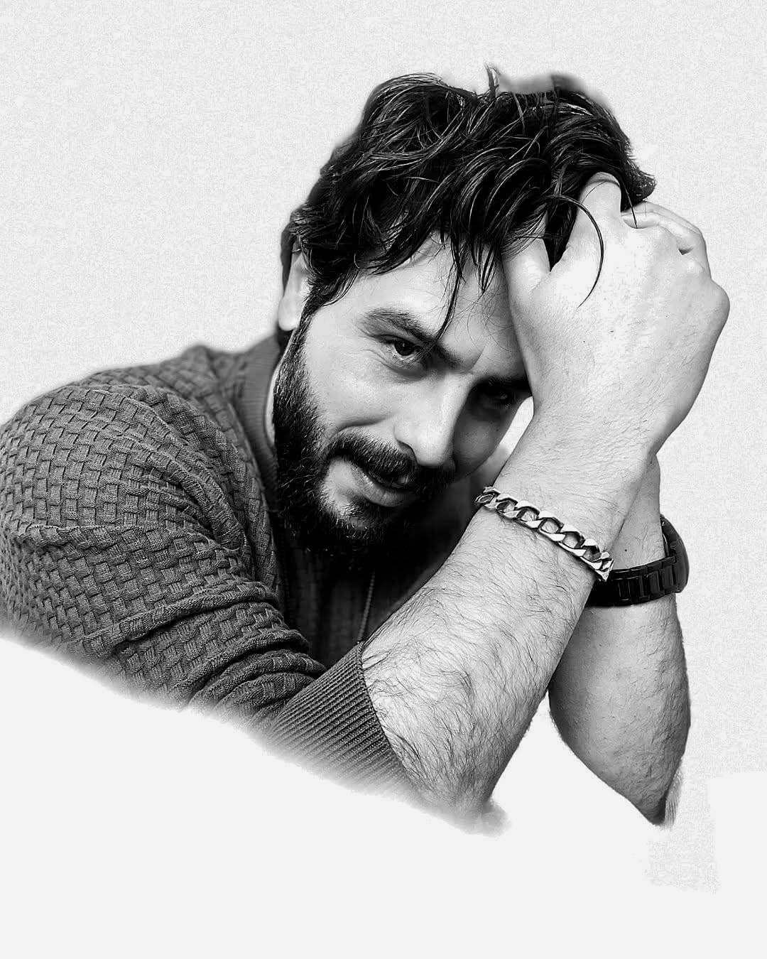 Bearded man in a textured sweater resting head on hands, black and white portrait.